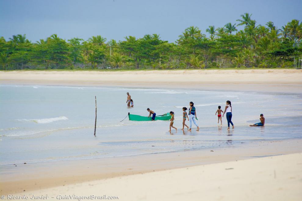 Imagem de mães com os filhos próximo ao barco de pescador na Praia Corumbau.